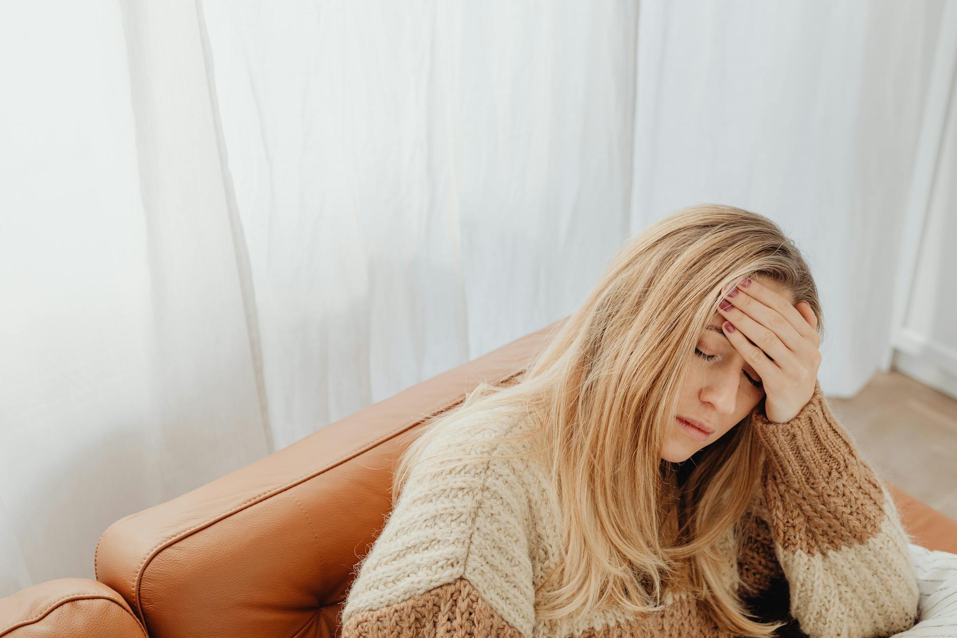 woman sitting on a couch with eyes closed and putting her hand on her forehead